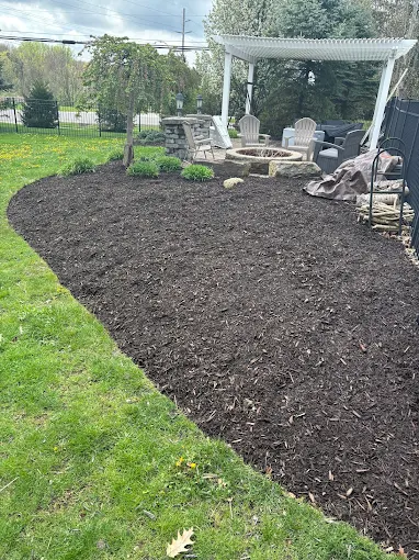 Backyard mulch bed surrounding a fire pit and pergola