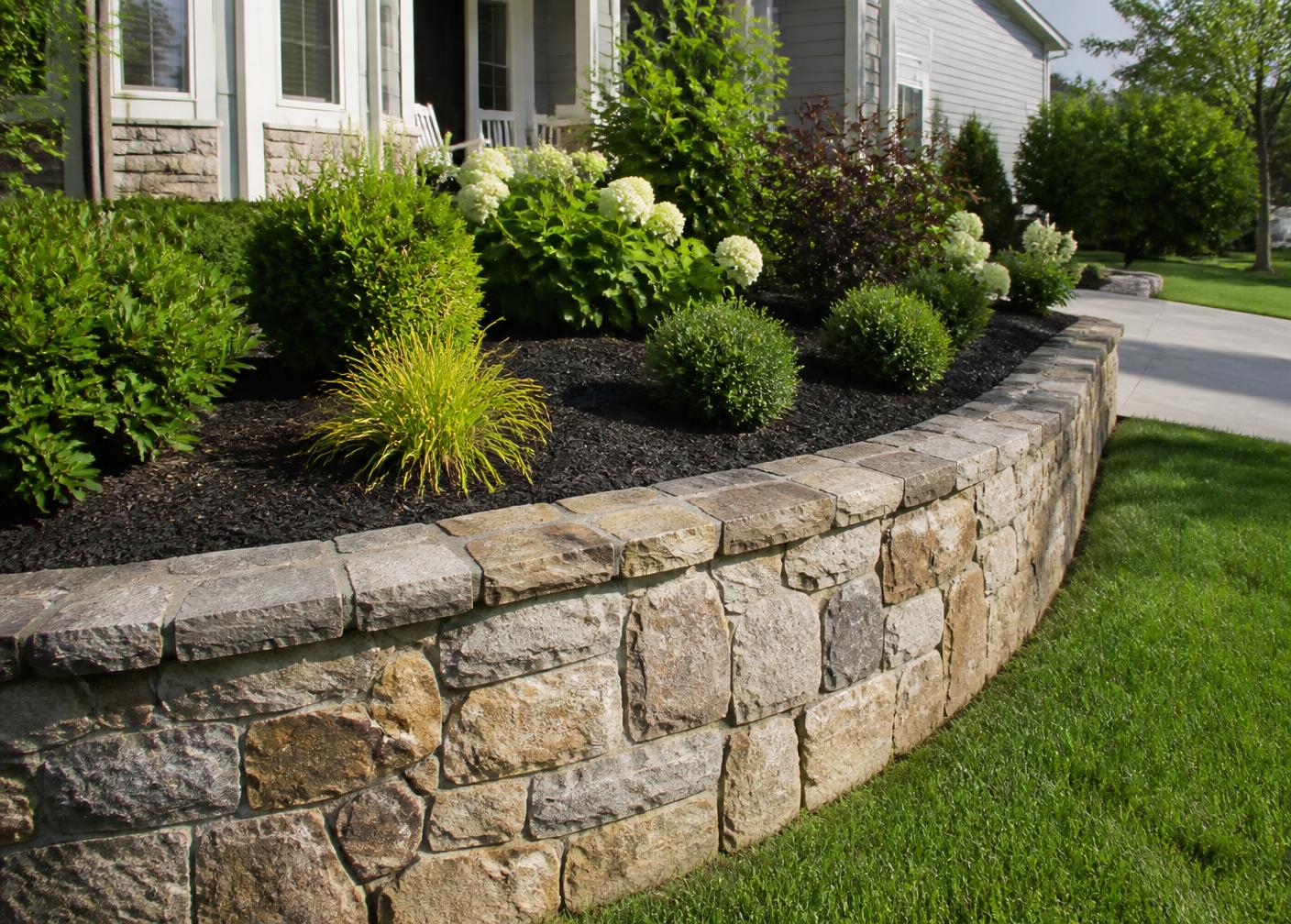 Curved natural stone retaining wall holding a front-yard planting bed